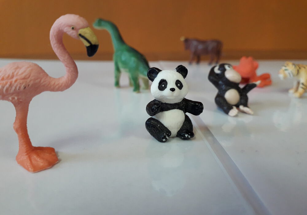 Spielfiguren stehen auf einem Tisch. In der Mitte ist ein Pandabär, links ein Flamingo und rechts ein Affe. Im Hintergrund unscharf sind weitere Tiere.